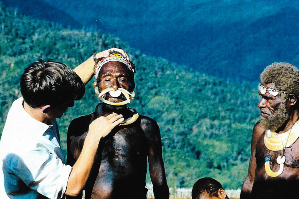 Two men stood in front of a hilly, countryside view. One man is wearing a traditional local headdress and the other is UK volunteer. 