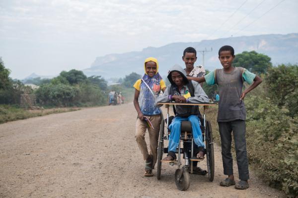 boy in wheelchair with three friends on a road that are helping to push him