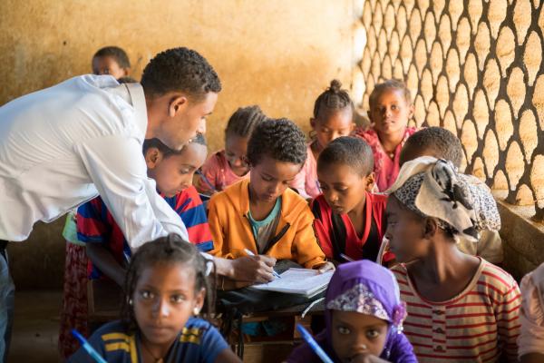 teacher stood in a classroom of young children, assisting them with work