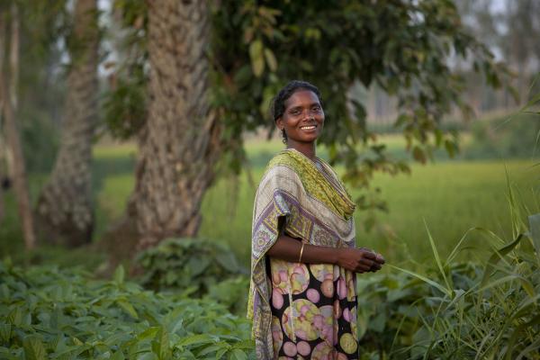 Farmer Selina Kerketa smiles as she stands on the edge of a green plantation in Durgapur Village, Rangpur, Bangladesh.