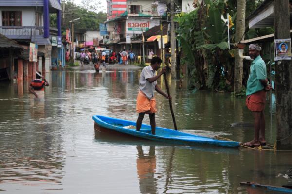 A man punts a boat down a flooded street in Kerala, India