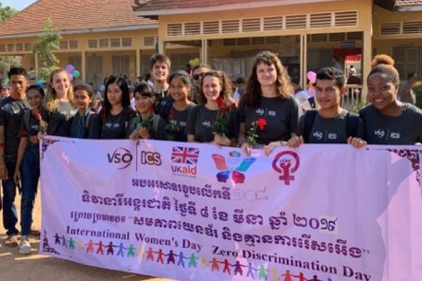 group of volunteers standing in front of a school holding a banner with cambodian writing